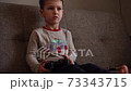 Little boy playing video game seated on a sofa 73343715