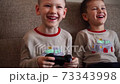 Two little brothers playing game console and laughing while sitting on sofa at home 73343998