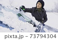 Woman cleaning snow from car window with brush 73794304