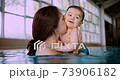 Mother blowing kisses on baby swimming in indoor pool 73906182
