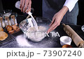 Close hand of professional chef man wear grey apron pours fresh milk into glass bowl with flour  73907240