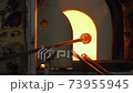 A glassblower or gaffer inserting melted hot glass into a traditional furnace. Rotating the metal pipe to create art with the precious material. A glassblowing factory in Murano, Venice. 73955945