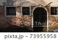 A romantic house front in Venice, Italy with sunlight reflections from water. An old traditional charming brick wall with windows and door open to the Venetian canal. Light dancing on surface. 4K. 73955958