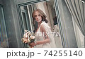 Young girl model demonstrates white wedding dress while standing in light room. 74255140