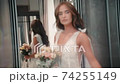 Woman wear wedding dress and pose, look at camera. Attractive model bride in room stand, bouquet 74255149