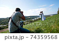 Professional wedding photographer taking pictures of the bride and groom on a hillside covered with green grass 74359568