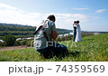 Professional wedding photographer taking pictures of the bride and groom on a hillside covered with green grass 74359569