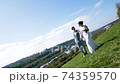 Professional wedding photographer taking pictures of the bride and groom on a hillside covered with green grass 74359570