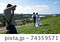 Professional wedding photographer taking pictures of the bride and groom on a hillside covered with green grass 74359571
