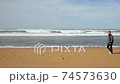 Man walking along the ocean on sandy beach 74573630