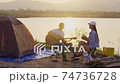 Young adult Asian couple playing guitar and drinking beer beside their tent campsite while sunset with dog. Tilt Down 74736728