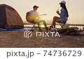 Young adult Asian couple playing guitar and drinking beer beside their tent campsite while sunset with dog. Crane shot. 74736729