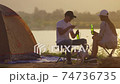 Young adult Asian couple Cheers and drink beer beside their tent campsite while sunset with Dog 74736735