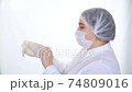 Young caucasian female doctor in protective mask and cap putting on white protective glove. Healthcare and medical concept 74809016
