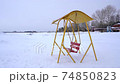 An old swing against the background of a snowy shore. 74850823