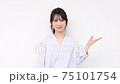 A young woman standing in front of a white wall and making a guiding gesture 75101754