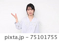 A young woman standing in front of a white wall and making a guiding gesture 75101755