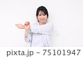 Young woman standing in front of a white wall and stretching 75101947