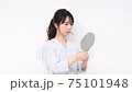 Young woman standing in front of a white wall and looking in the mirror 75101948
