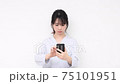A young woman standing in front of a white wall and using a smartphone 75101951