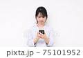 A young woman standing in front of a white wall and using a smartphone 75101952