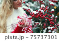 Girl on the street on the background of Christmas trees and red berries 75737301