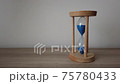 Pouring sand in an hourglass standing on an a wood desk. 75780433