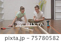 Young beautiful couple improve the room in new home. Man and woman together assemble furniture according to instructions while sitting on floor in living room. 75780582
