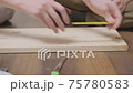 Close-up of hands of man and woman using tape measure and pencil mark on wooden shelf for assembling bookcase or cabinet while sitting on floor in room of house or apartment. Home improvement. 75780583