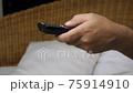Close-up of a hand with TV remote controller switching TV channels. Slow motion 75914910