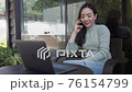 Asian woman freelance talking on mobile phone while typing on laptop in coffee shop. 76154799