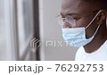 Concerned pensive look of an African American in a protective mask looking out the window. Coronavirus prevention concept, medical mask. Virus protection. 76292753