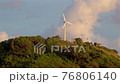 A lonely wind power generator standing on a mountain in a thicket of trees against a background of blue sky and beautiful cumulus clouds. Thailand, Phuket, Naiharn beach. 76806140