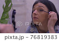 Attractive european brunette girl is doing makeup. Girl paints her eyelashes. Closup shot 76819383