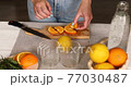 Female hand cut orange, Woman preparing, makFemale hand cut orange, Woman preparing, making ing citrus and rosemary fresh lemonade in glass on a white table at home, summer drink, detox healthy water. 77030487