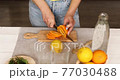 Female hand cut orange, Woman preparing, makFemale hand cut orange, Woman preparing, making ing citrus and rosemary fresh lemonade in glass on a white table at home, summer drink, detox healthy water. 77030488