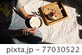 Woman in jeans sitting on the bed, and eating healthy granola bowl during the morning sunlight, breakfast in the bed. 77030522