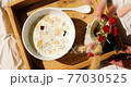 Breakfast in bed, female hands put try with bowl muesli, granola and flower in sunlight at home, chambermaid bringing tray with breakfast in hotel room, good service 77030525
