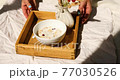 Breakfast in bed, female hands put try with bowl muesli, granola and flower in sunlight at home, chambermaid bringing tray with breakfast in hotel room, good service 77030526
