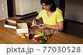 Woman reading a recipe from a meal kit box near of fresh ingredients order from a meal kit company, delivered, cooking at home. 77030528