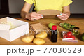 Woman reading a recipe from a meal kit box near of fresh ingredients order from a meal kit company, delivered, cooking at home. 77030529