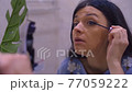 Attractive european brunette girl is doing makeup. Girl paints her eyelashes. Closup shot 77059222