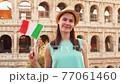 Portrait of young woman in hat on vacation in Rome. Female tourist near Colosseum wave italian flag 77061460