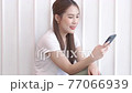 Smiling happy beautiful Asian woman relaxing using technology of phone near white wall at home 77066939