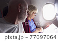 Senior couple flying in airplane in daytime. Pensioners reading inflight magazine near window 77097064