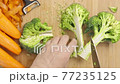 Man hands slice Broccoli on chopping board framed by fresh vegetables on the table - top view, flat lay 77235125