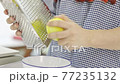 A young woman is using a cheese grater to grate lemon zest in her home kitchen. 77235132