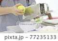 A young woman is using a cheese grater to grate lemon zest in her home kitchen. 77235133