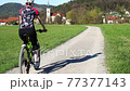 Woman cycling along sand-gravel road. 77377143