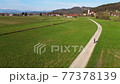 Woman cycling along dirt road across the Slovenian meadow. 77378139